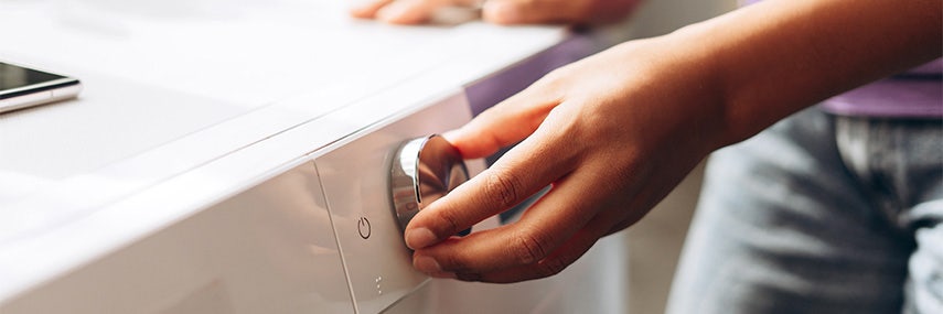 Vrouwelijke hand draait aan knop van wasmachine om juiste wasprogramma in te stellen. Vrouwelijke hand draait aan knop van wasmachine om juiste wasprogramma in te stellen.