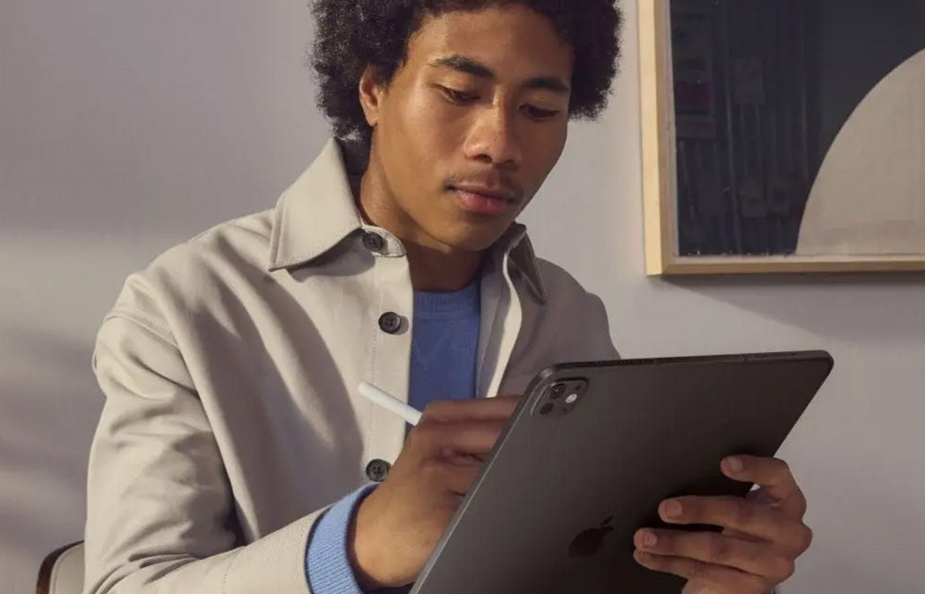 Man zit in woonkamer met een donkergrijze Apple iPad in zijn hand te tekenen met een stylus pen. Man zit in woonkamer met een donkergrijze Apple iPad in zijn hand te tekenen met een stylus pen.