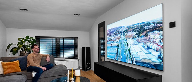 Man zit op de bank in de woonkamer een film te kijken op een 98 inch televisie.
