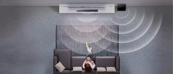 Vrouw zit op de bank voor de televisie en de soundbar laat de surroundervaring zien.