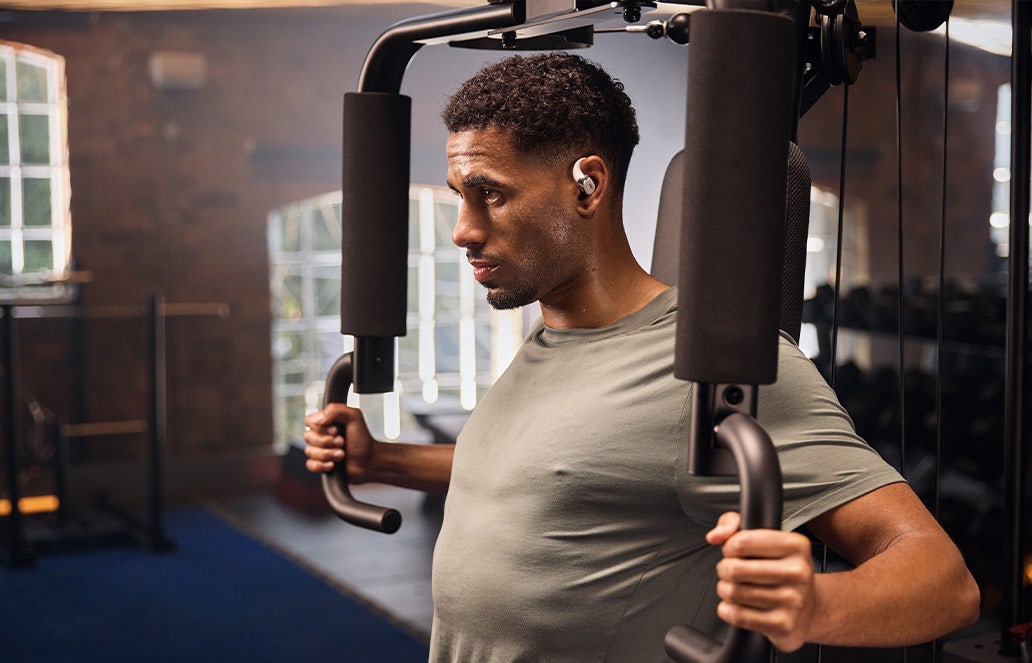 Man staat in sportschool te sporten met Shokz OpenRun Pro2 in.