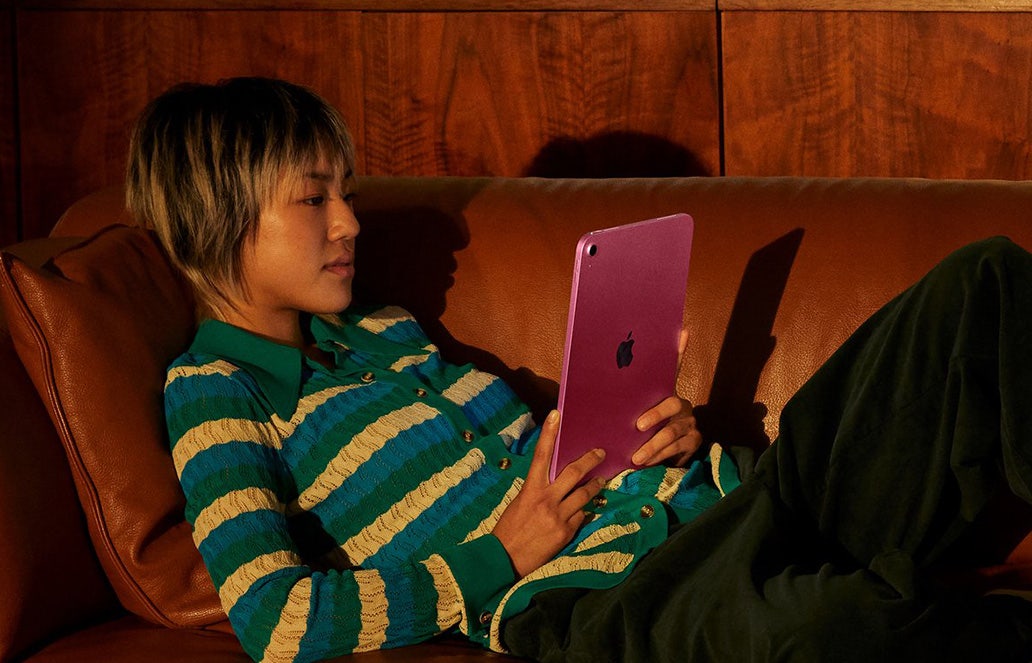 Vrouw ligt op de bank met een roze Apple iPad in haar handen, een filmpje te kijken. Vrouw ligt op de bank met een roze Apple iPad in haar handen, een filmpje te kijken.