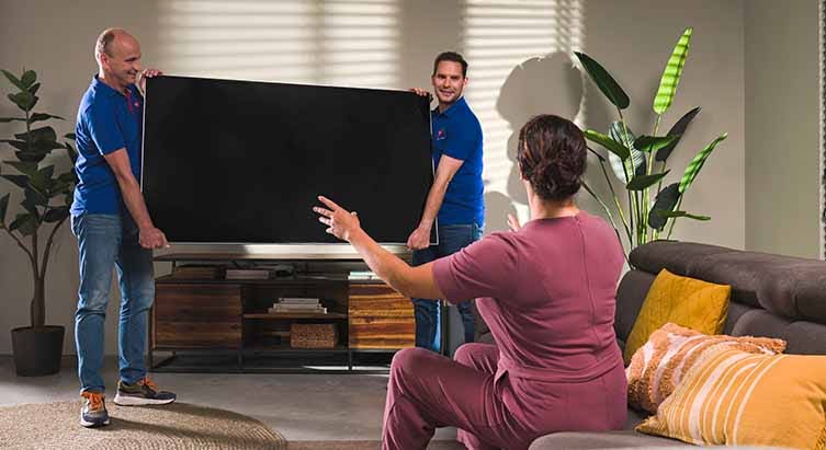 Twee vakmannen van Electro World installeren televisie bij klant thuis. Twee vakmannen van Electro World installeren televisie bij klant thuis.